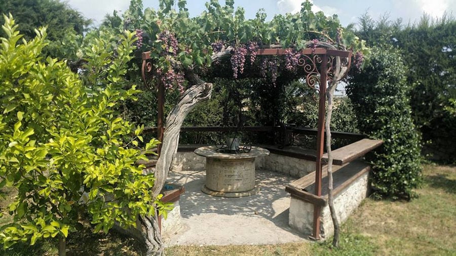 stone fountain surrounded by wood benches and trees at 'Marianna' garden